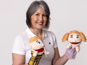 Woman holding two puppets and smiling.
