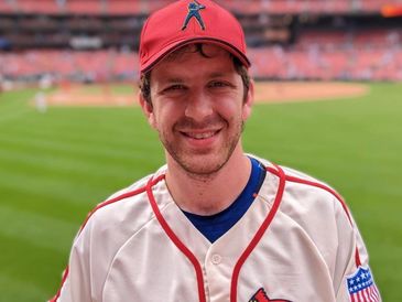 Smiling man in a baseball uniform at a stadium.