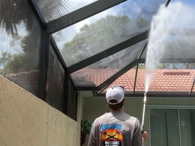 Man pressure washing a screened roof.