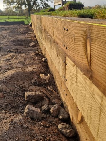 New wooden retaining wall with grass and a bench above it.