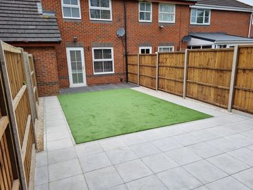 A backyard with artificial grass and paved tiles surrounded by wooden fences.