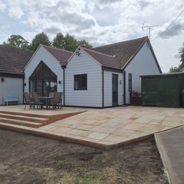 Modern patio with outdoor seating in a spacious backyard of a white house.
