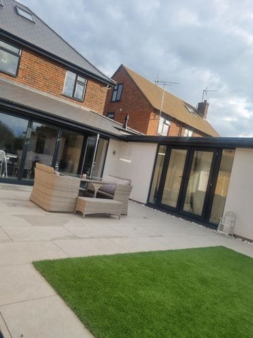 Modern patio with wicker furniture and green lawn under a cloudy sky.