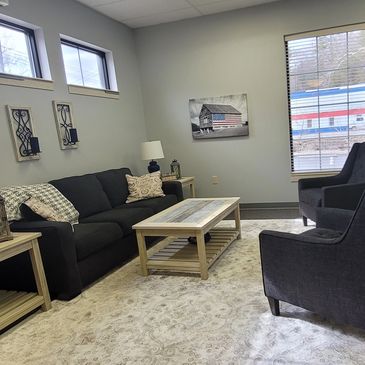 Picture of room with grey wall and black chairs and couch. There is also a coffee table. 
