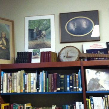 genealogy books on dark wooden shelf with vintage pictures hung on wall