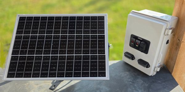 Small solar panel and control box on a metal surface outdoors.