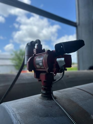 Close-up of a red Fill-Rite fuel pump nozzle on a tank under a blue sky.
