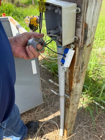 Person wiring an outdoor electrical outlet on a wooden post.