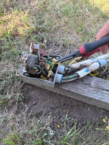Hand using pliers to manipulate wires in a damaged outdoor electrical box.
