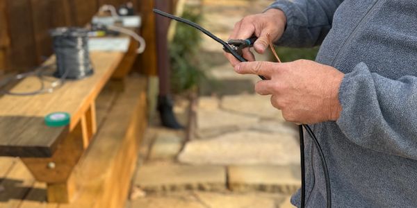 Person stripping wire insulation outdoors near a wooden deck.