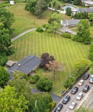 A suburban house with a large striped lawn and cars lined up on the street.