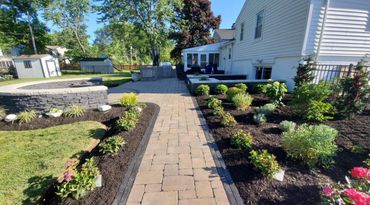 A landscaped backyard with a stone pathway, garden beds, and a patio area.