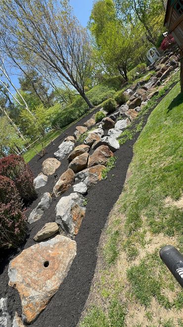 Rock garden with mulch and greenery under a clear blue sky.