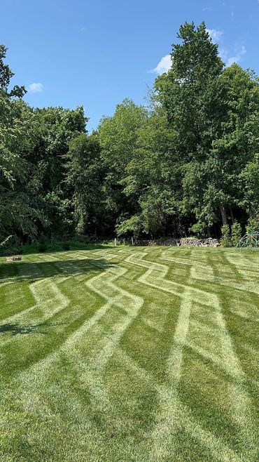 Lawn with intricate zigzag mowing patterns under clear blue sky.