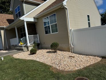 House exterior with a rock garden and two small bushes under a window.