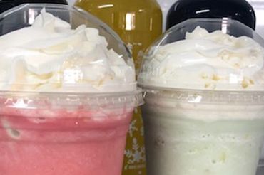 Two creamy blended drinks topped with whipped cream in plastic cups.