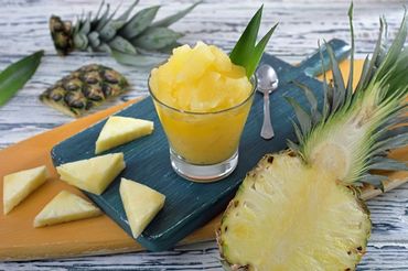 Glass of pineapple sorbet with fresh pineapple slices on cutting boards.