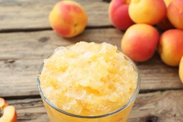 Glass of apricot granita with fresh apricots on wooden table.