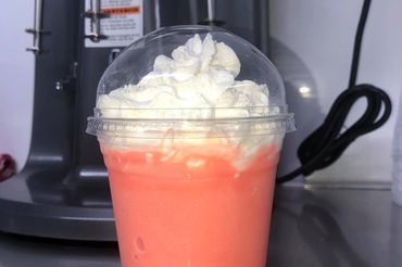 A pink blended drink topped with whipped cream in a plastic cup.