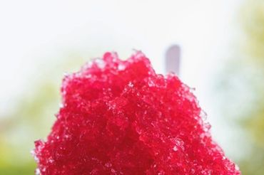 A vibrant red shaved ice in a white cup on a sunny day.