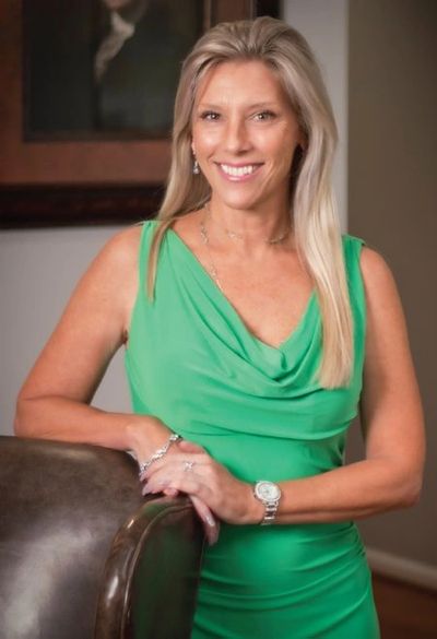 Smiling woman in a green dress leaning on a chair indoors.