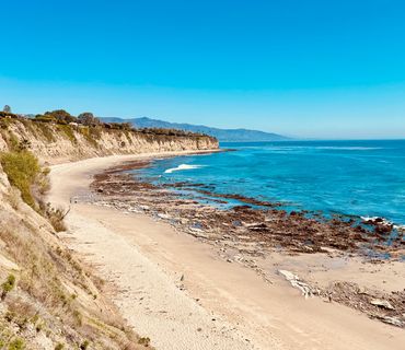 Sunny coastal beach with clear blue sky and waves.