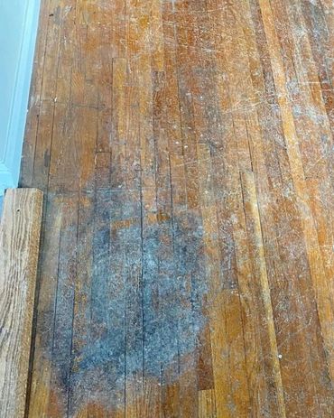 Worn and stained hardwood floor with visible damage.