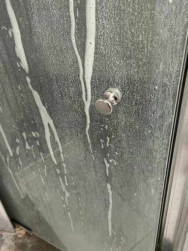 Close-up of a soap-covered glass shower door. BEFORE clean