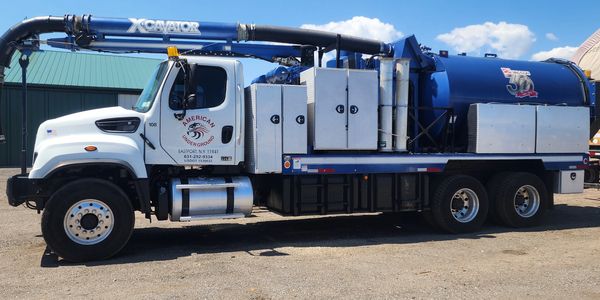 Large white and blue industrial vacuum truck parked outside on a sunny day.