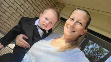 Woman smiling while holding a toddler dressed in a suit and tie.