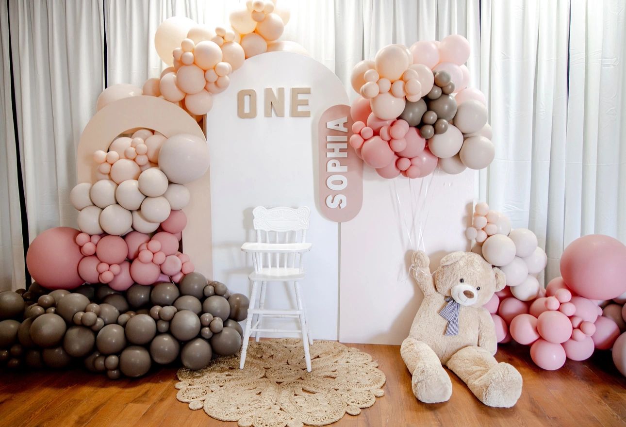Elegant first birthday setup with pastel balloons and a teddy bear.