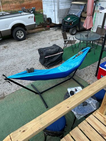 Blue hammock on a black stand in an outdoor setting with chairs and a golf cart.