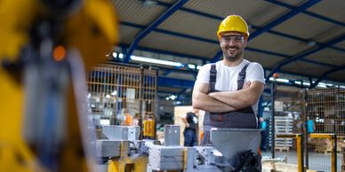 Smiling factory worker in safety gear standing confidently in industrial setting.