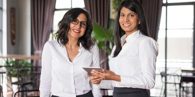 Two professional women smiling in an office setting, one holding a tablet.