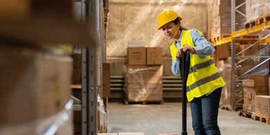 Woman in safety gear operating pallet jack in warehouse.