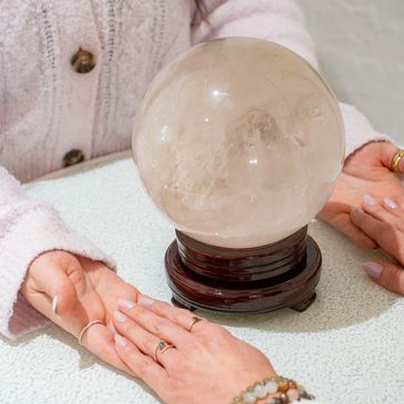 2 women hold hands as renee gives an akashic record reading with a crystal ball on the table