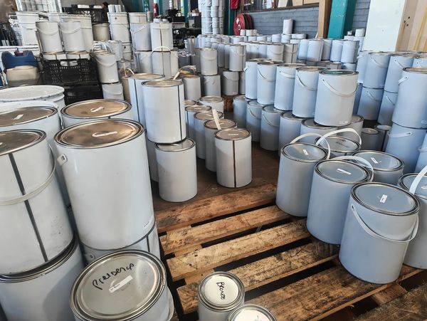 Many white paint cans stacked on wooden pallets inside a warehouse.