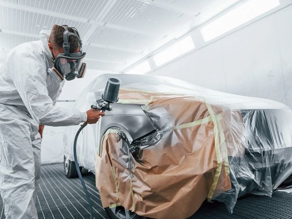 Man spray painting a car in a protective suit.