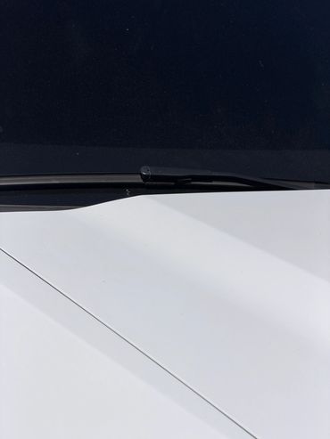 Close-up of a black windshield wiper on a white car hood.