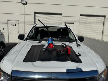 White truck with windshield glass removed and tools on the hood.