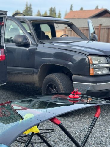 A black truck with a removed windshield and a replacement windshield on a stand.