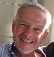 Smiling older man with gray hair and beard in casual shirt.