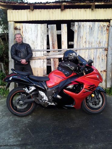 Man in black leather jacket stands next to red and black sport motorcycle.