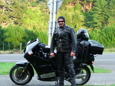 Man in leather motorcycle gear standing beside a black BMW motorcycle.