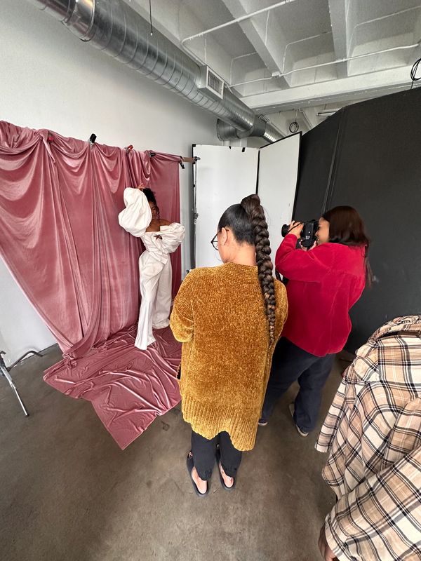 Fashion photoshoot with a model posing against a pink velvet backdrop.