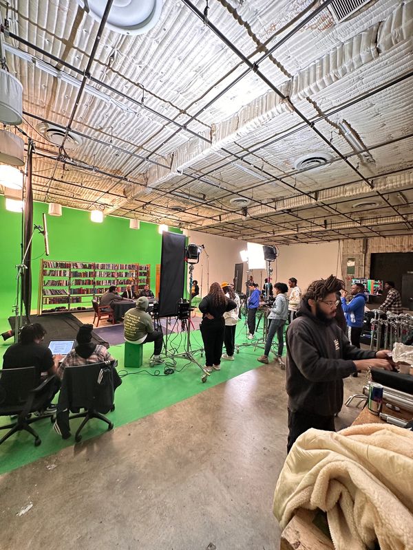Film crew working on a green screen set with actors and equipment.