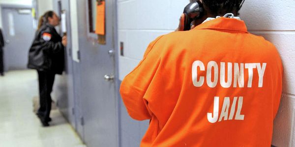 Inmate in orange jumpsuit labeled 'County Jail' making a phone call.