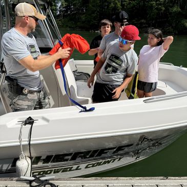 Sheriff and kids on boat during safety demonstration by the water.