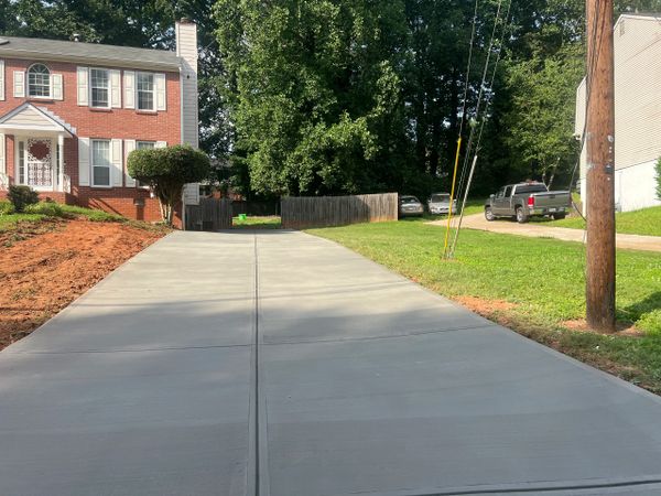 Newly paved driveway leading to a brick house with greenery.