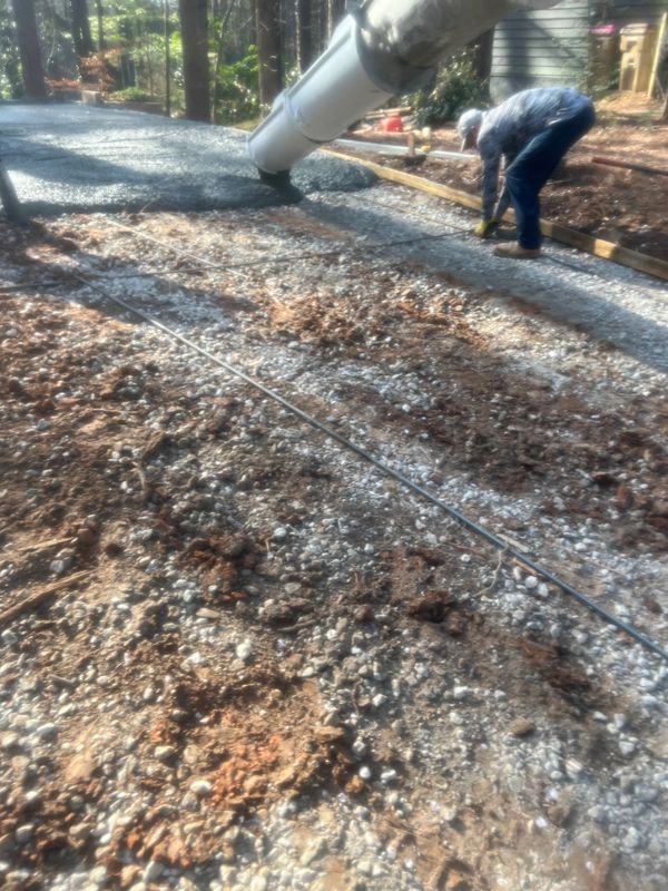 Worker pours concrete for a new driveway on a sunny day.